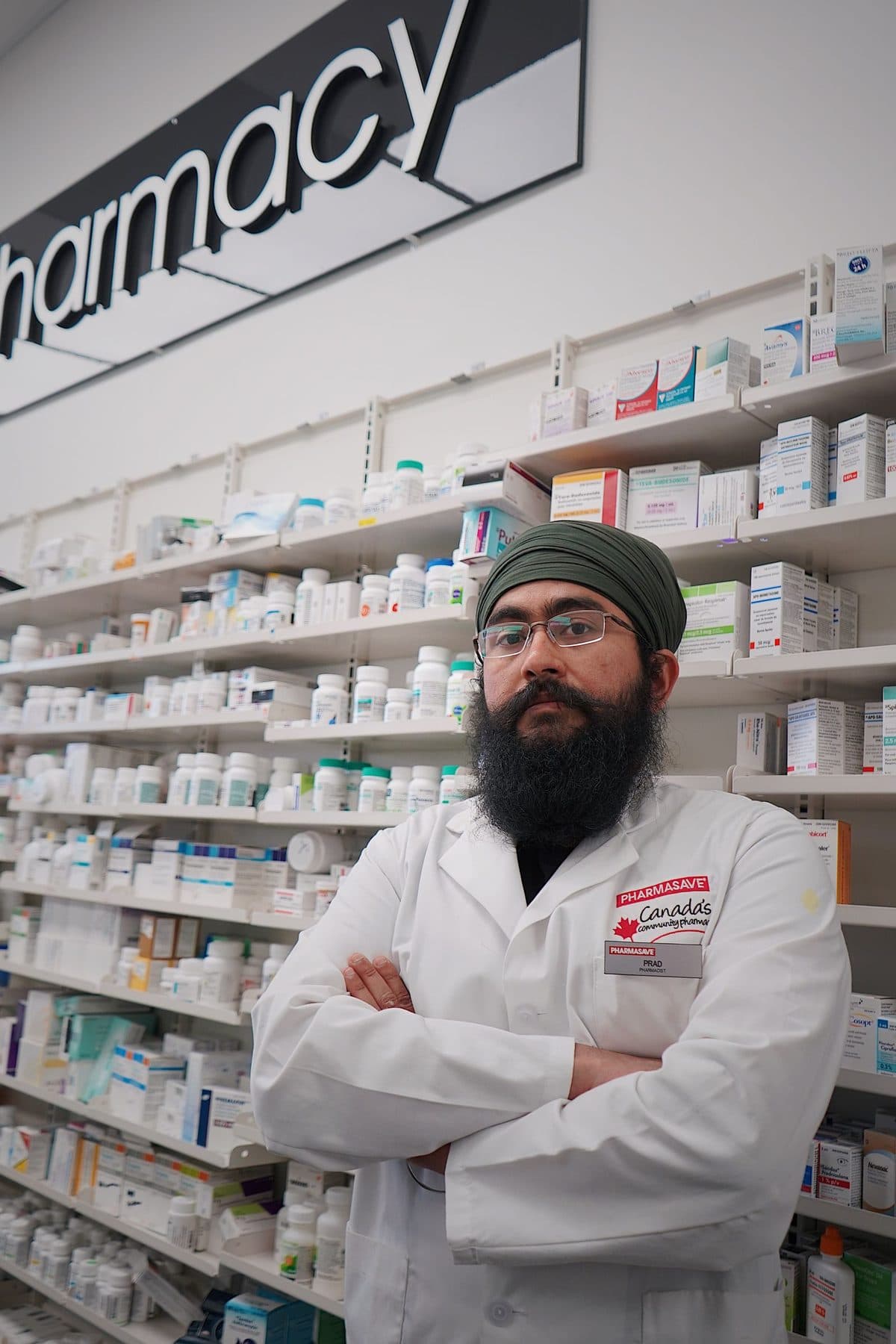 Farmacêutico de jaleco diante das prateleiras de uma farmácia
